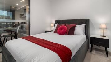 A modern bedroom with a large bed, a red throw blanket, and two bedside lamps.