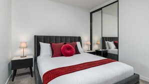 Un dormitorio moderno con una cama grande, una mesita de noche, una lámpara y un espejo.