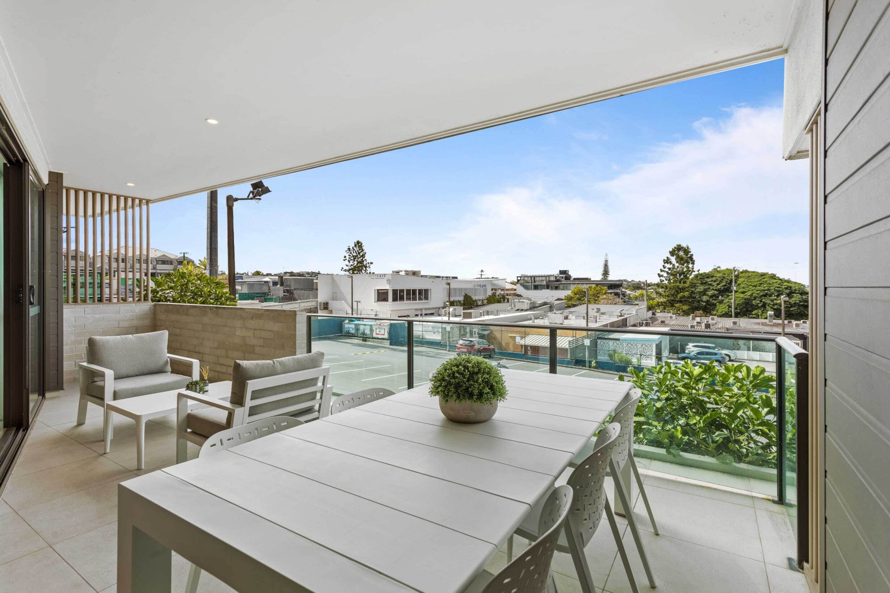 A balcony with a table and chairs, a potted plant, and a view of the cityscape.