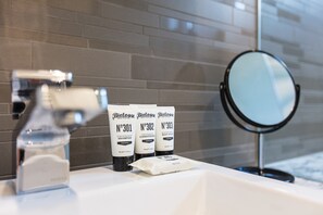Een badkamermeubel met een wastafel, een spiegel en drie flessen Biolgy shampoo.
