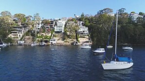 En småbåtshamn med flera båtar förtöjda, omgiven av bostadshus och frodig grönska.