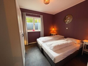 A bedroom with two beds, a window with curtains, a bedside lamp, and a wall-mounted artwork. - Zilverspar | Sfeervolle bosvilla met barrelsauna | Putten, Veluwe (Putten)