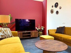 A living room with a flat-screen TV, yellow sofas, a wooden coffee table, and a red accent wall. - Zilverspar | Sfeervolle bosvilla met barrelsauna | Putten, Veluwe (Putten)