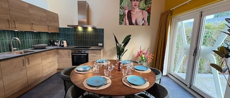 Una cocina moderna con armarios de madera, una mesa de comedor preparada para seis personas y un ventanal con vistas a zonas verdes.