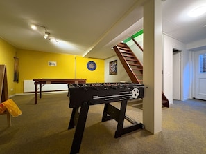 Una habitación con mesa de futbolín, dardos y una escalera.