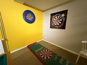 Ein Zimmer mit Dartscheibe an der Wand, einem Teppich mit Dartmuster und einem weißen Stuhl.