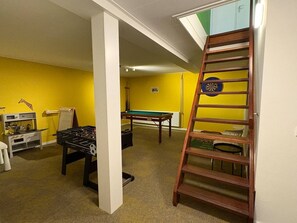 Ein Zimmer mit Kicker- und Billardtisch sowie einer Schlafgalerie mit Zugang über eine Leiter.