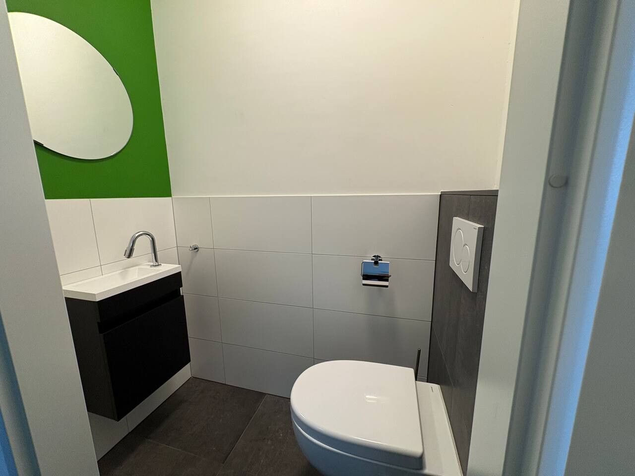 A compact bathroom with a white sink, black cabinet, and a white toilet.