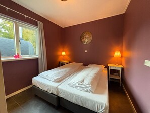A bedroom with two beds, a window with curtains, and two bedside lamps.