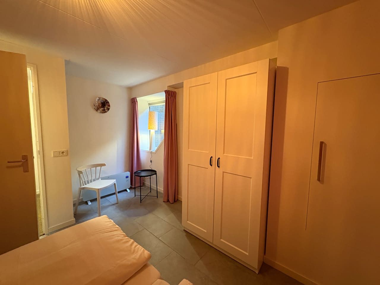 A bedroom with a bed, a chair, a small table, and a wardrobe.