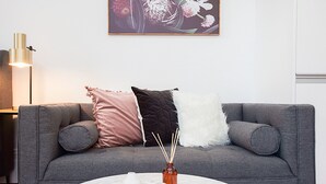 A grey sofa with three pillows, a white vase with reed sticks, and a white tray with a candle. - Comfortable Renovated Studio Close To City (Sydney)