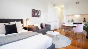 A modern hotel room with a large bed, a sofa, a dining table with chairs, and a kitchen area. - Comfortable Renovated Studio Close To City (Sydney)