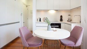 A modern kitchen with white cabinets, a white dining table with two purple chairs, and a small plant on the table. - Comfortable Renovated Studio Close To City (Sydney)