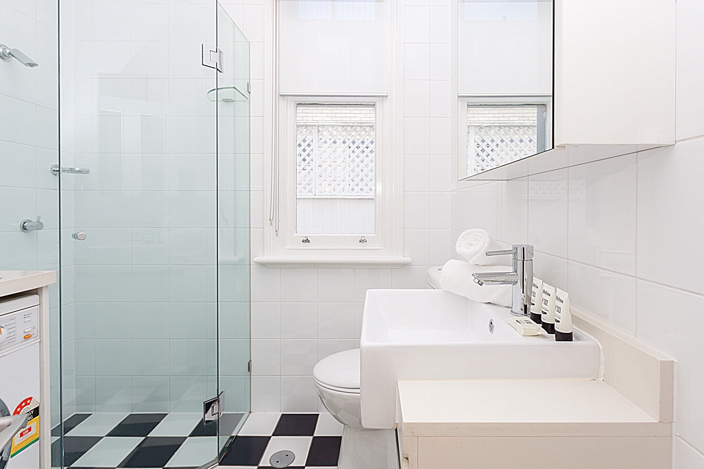 Un baño moderno con cabina de ducha de vidrio, inodoro blanco y lavabo con espejo superior.