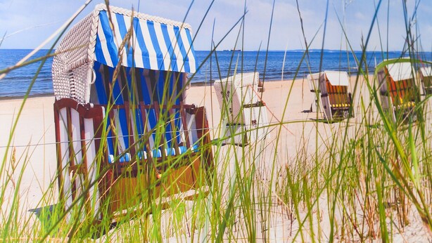 Een strand met een gestreepte strandstoel en een rieten stoel.