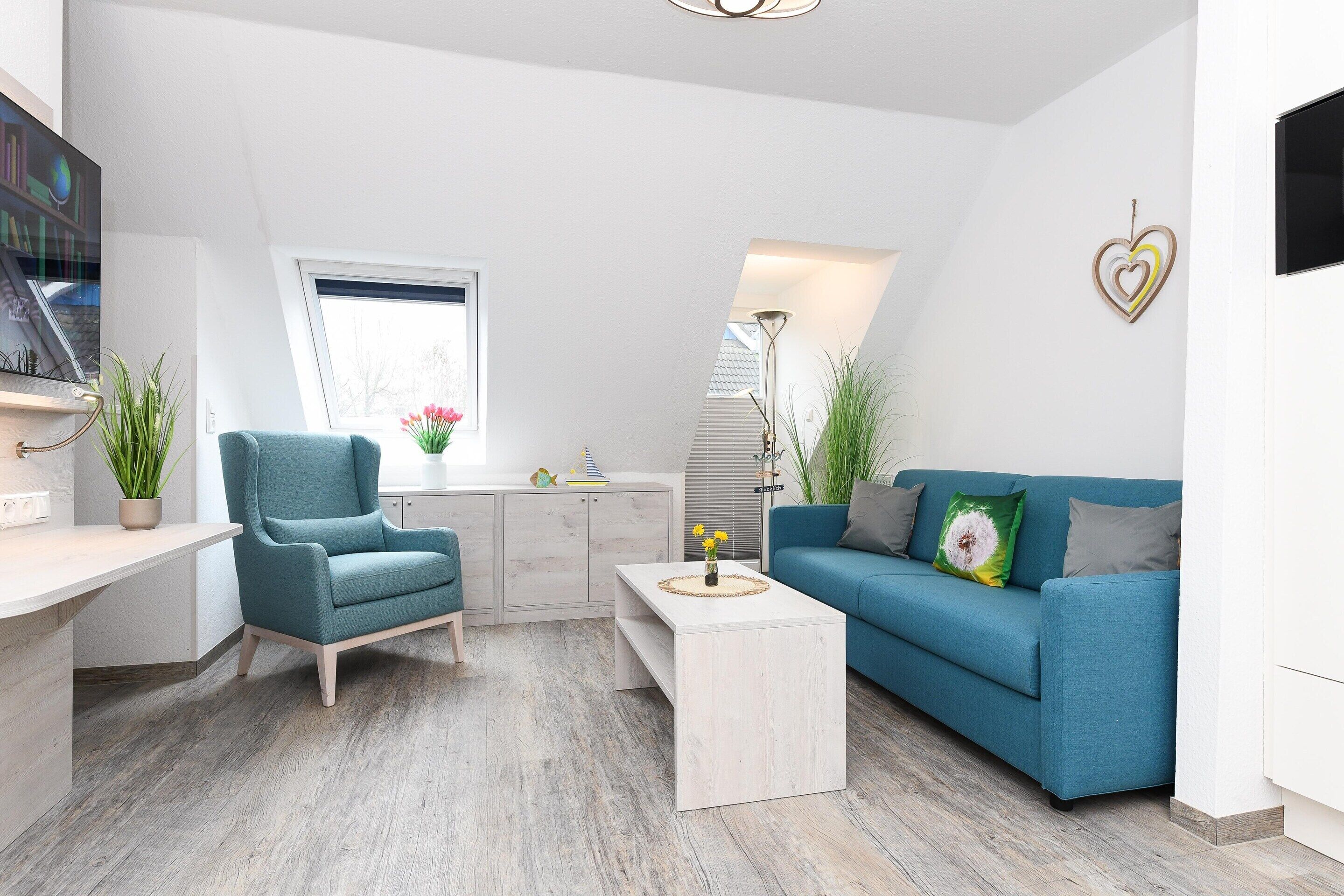 A modern living room with a blue sofa, a teal armchair, a coffee table, and a white desk.