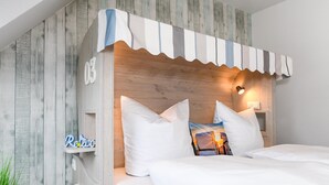 Een slaapkamer met een houten hoofdeinde, wit beddengoed en een klein plankje met een bordje.