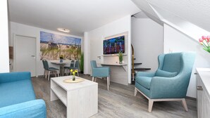 Een moderne woonkamer met een bank, stoelen, een salontafel en een aan de muur bevestigde televisie.