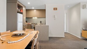 A modern kitchen with wooden cabinets, a central island, and a dining area with a wooden table and chairs. - Gorgeous 3-bed Apartment Near Flagstaff Gardens (Melbourne)