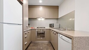 A compact kitchen with a built-in oven, microwave, and dishwasher, featuring light-colored cabinets and a granite countertop. - Gorgeous 3-bed Apartment Near Flagstaff Gardens (Melbourne)