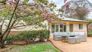 A house with a patio area featuring outdoor furniture and a tree with pink flowers. - Stunning Katoomba Home With Lush Garden&playground (Katoomba)