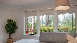 A room with a grey sofa, a potted plant, and large windows with a view of greenery outside. - Stunning Katoomba Home With Lush Garden&playground (Katoomba)