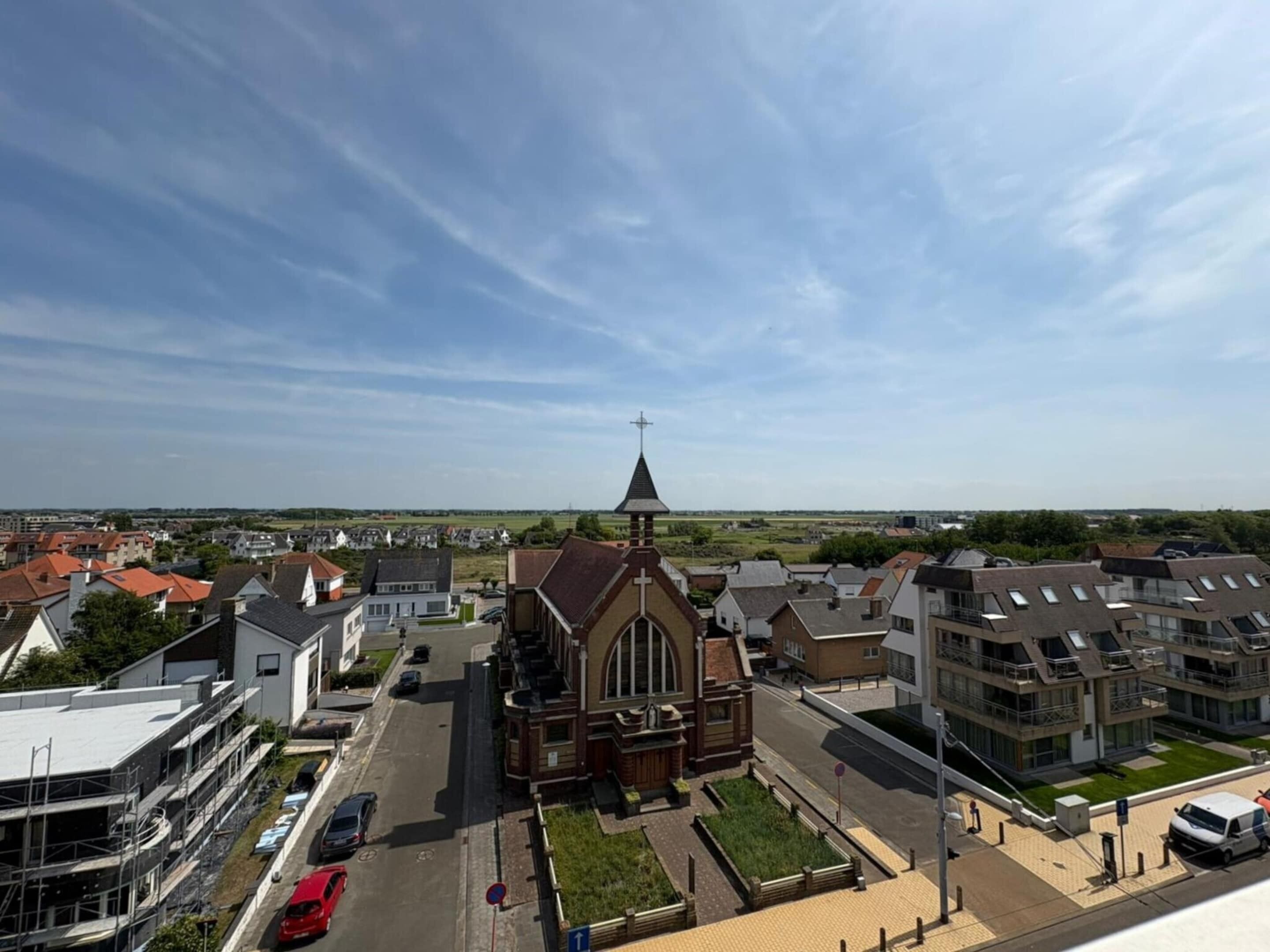 Een kerk met een opvallende kerktoren in een woonwijk met moderne huizen.