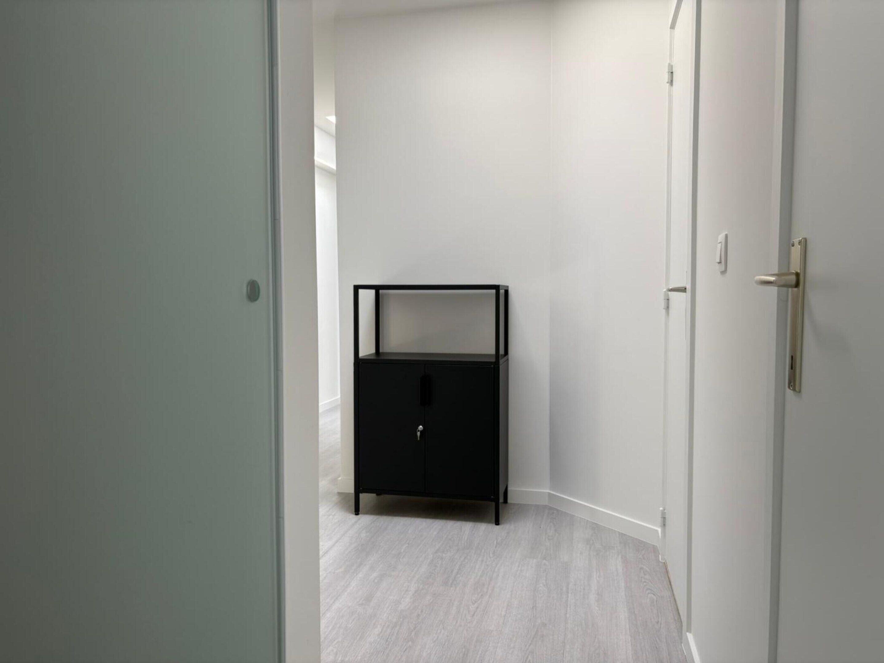 Ein Flur mit einem schwarzen Schrank, weißen Wänden und einem grauen Boden.