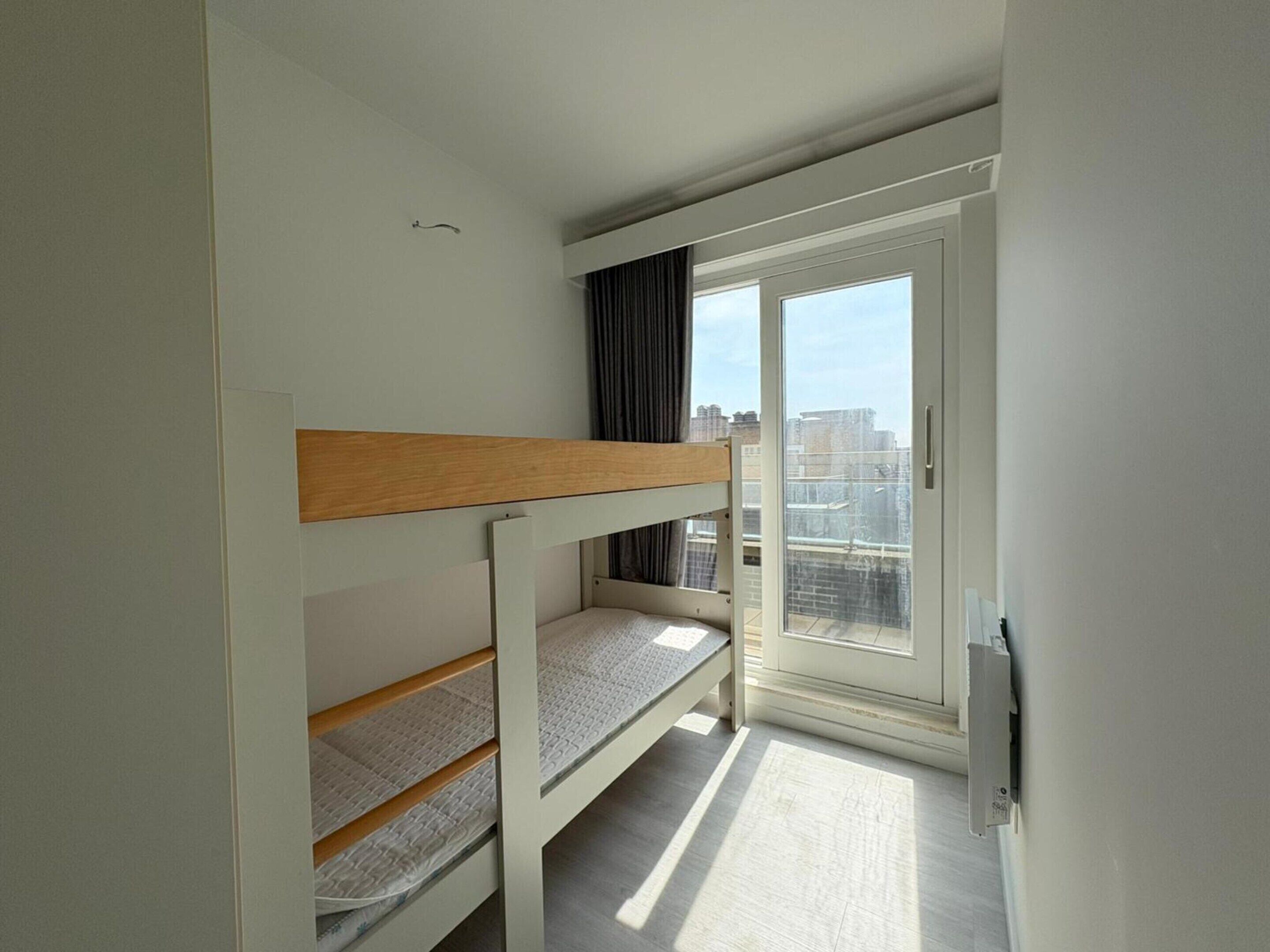Una habitación pequeña y moderna con literas, una puerta corrediza de vidrio a un balcón y vistas a la ciudad.