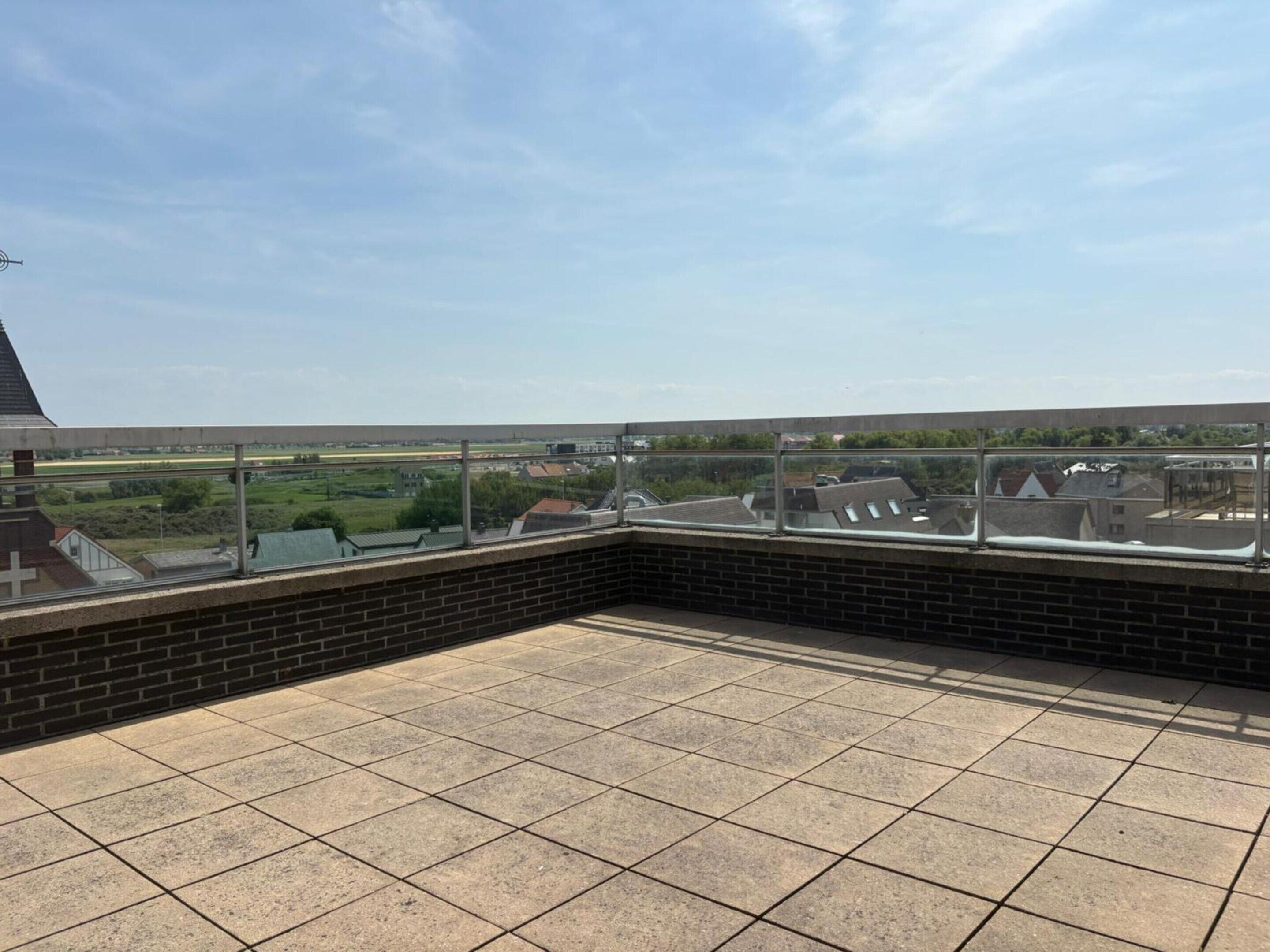 Een terras op het dak met een helder uitzicht over het omliggende landschap, inclusief huizen en een groen veld.