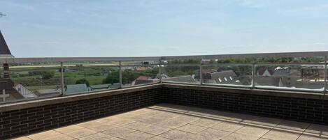 Een terras op het dak met een helder uitzicht over het omliggende landschap, inclusief huizen en een groen veld.