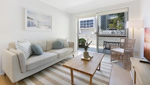 A modern living room with a sofa, coffee table, and wicker chair. - Ground Floor 2-bed Mermaid Beach Pad With Parking (Gold Coast)
