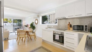 A modern kitchen with white cabinets, a microwave, and an oven. There is a dining area with a table and chairs. - Ground Floor 2-bed Mermaid Beach Pad With Parking (Gold Coast)