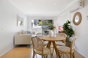 Un salon moderne avec un canapé, une table à manger et des chaises, ainsi qu’une grande fenêtre.