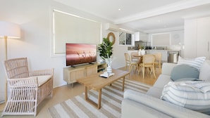 A modern living room with a wooden coffee table, a sofa, a wicker chair, and a television. - Ground Floor 2-bed Mermaid Beach Pad With Parking (Gold Coast)