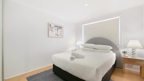 A modern bedroom with a large bed, bedside tables, a mirror, and a framed picture on the wall. - Ground Floor 2-bed Mermaid Beach Pad With Parking (Gold Coast)