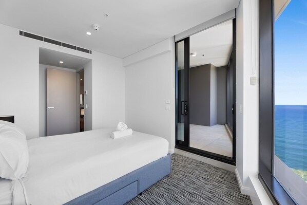 A modern hotel room with a large bed, a walk-in closet, and a balcony with a view of the ocean. - Luxe Oceanfront 1-bed High Rise With Pool & Gym (Gold Coast)