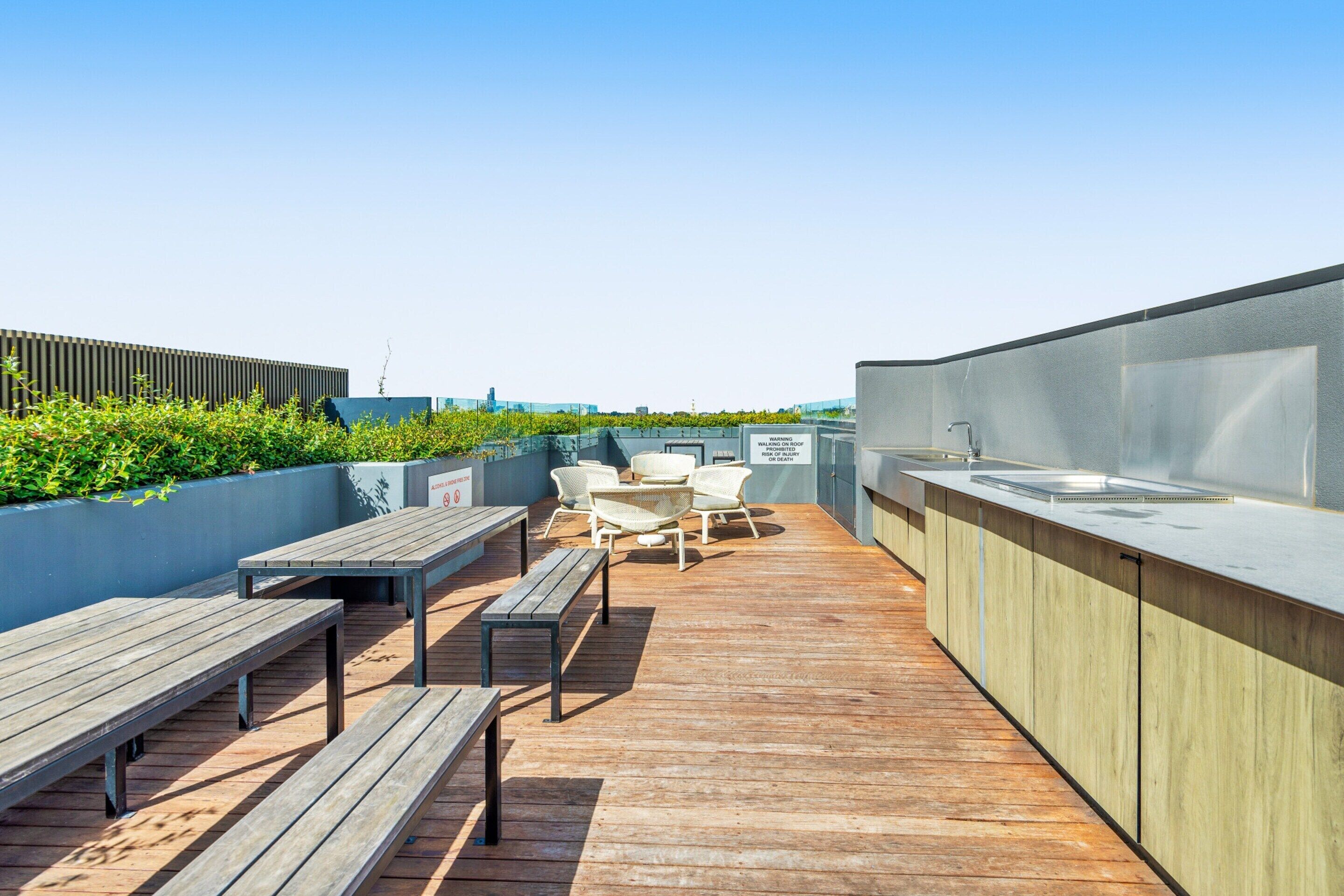 Terraza en la azotea con bancos de madera, una mesa, sillas, zona de bar y vistas del horizonte urbano.
