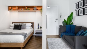 A bedroom with a wooden bed, a bedside table with a lamp, and a shelf with books and plants. - Stylish Studio Near Kings Cross Train Station (Sydney)