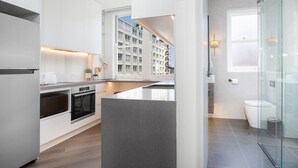 A modern kitchen with white cabinetry, a built-in oven, and a large window overlooking a residential area. - Stylish Studio Near Kings Cross Train Station (Sydney)