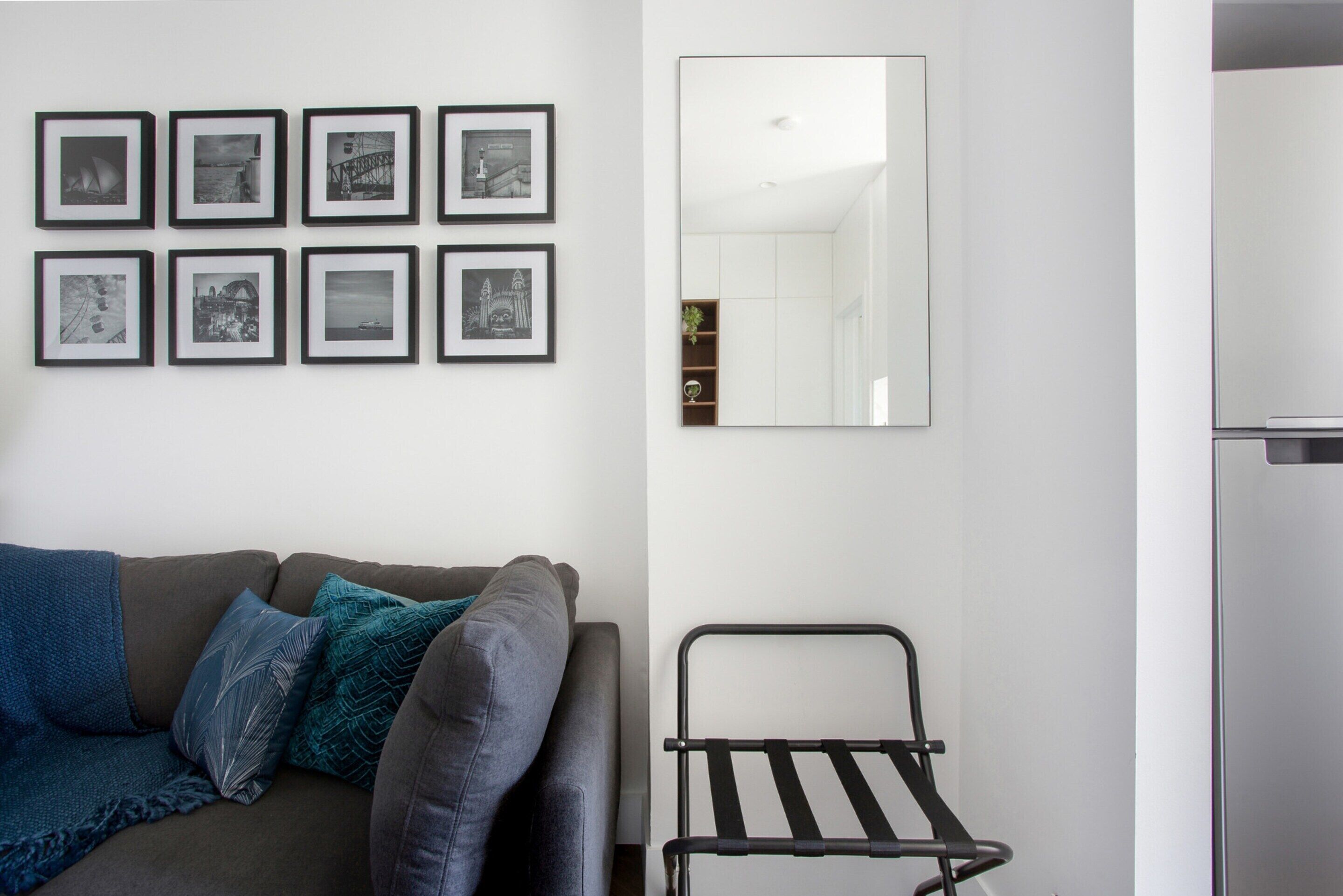 Een moderne woonkamer met een grijze bank, blauwgroene kussens, een zwart metalen rek en negen ingelijste foto's aan de muur.