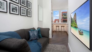 A living room with a sofa, framed pictures on the wall, and a large TV displaying a beach scene. - Stylish Studio Near Kings Cross Train Station (Sydney)