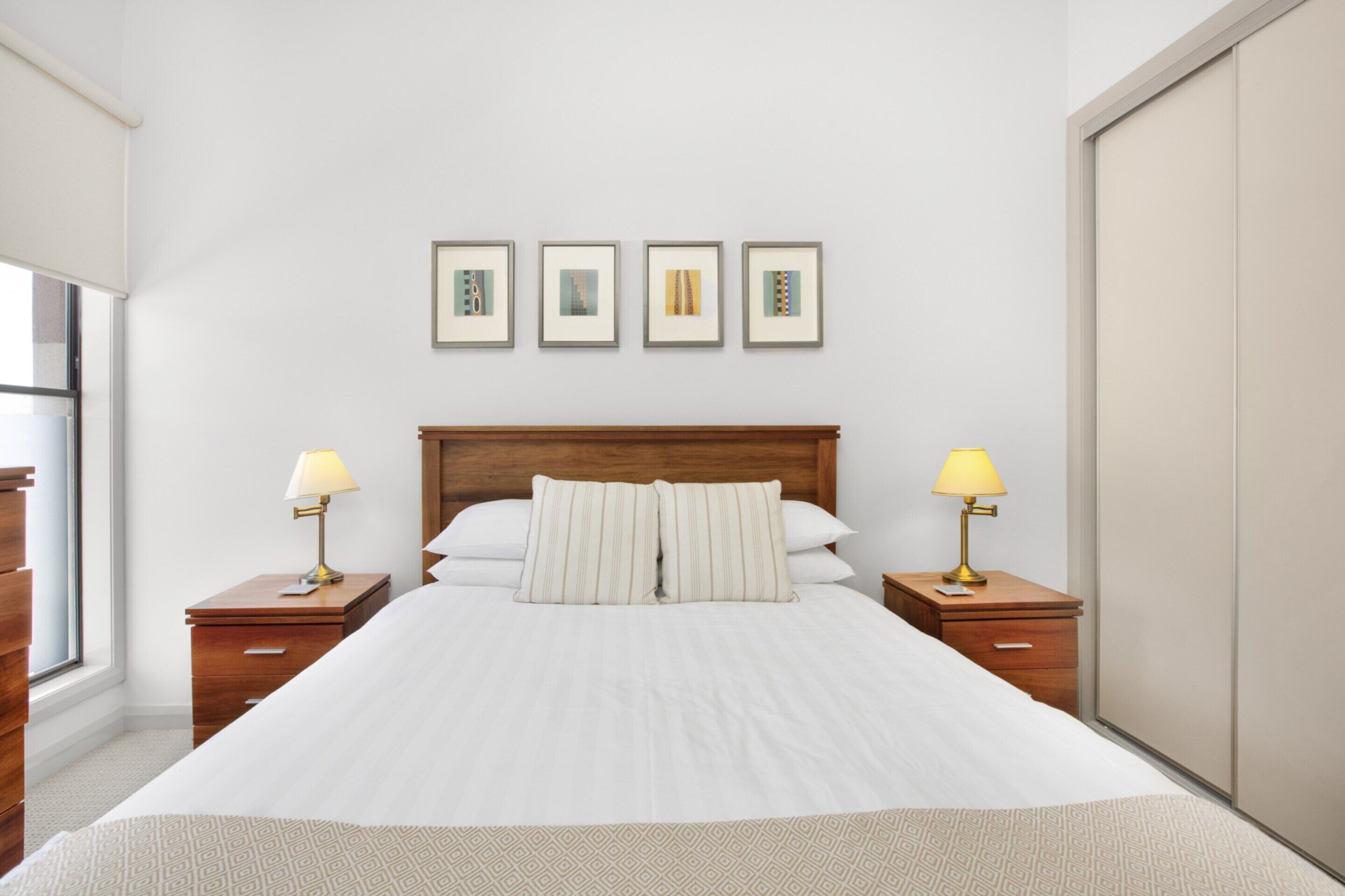 A neatly made bed with a wooden headboard, two bedside tables with lamps, and four framed pictures on the wall.