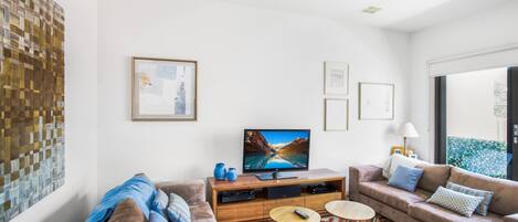 A modern living room with a large flat-screen TV, two sofas, a coffee table, and a patterned rug.