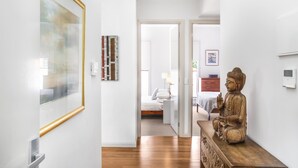 A hallway with a wooden floor, a statue, and a bed in the background. - 2-bed Apartment With Parking & Balcony Near Trains (Melbourne)