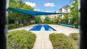 A swimming pool with a blue tarp overhead, surrounded by greenery and a paved walkway. - Tranquil 1-bed Apartment With Courtyard, Pool, BBQ (Canberra)