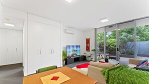A modern living room with a dining area, large windows, and a view of the outdoors. - Tranquil 1-bed Apartment With Courtyard, Pool, BBQ (Canberra)