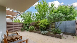 A patio with wooden furniture, a tiled floor, and a variety of plants and trees. - Tranquil 1-bed Apartment With Courtyard, Pool, BBQ (Canberra)