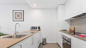 A modern kitchen with a stainless steel sink, a microwave, a stove, and a trash bin. - Tranquil 1-bed Apartment With Courtyard, Pool, BBQ (Canberra)