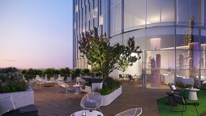 A rooftop terrace with outdoor seating, a tree, and a glass building in the background.